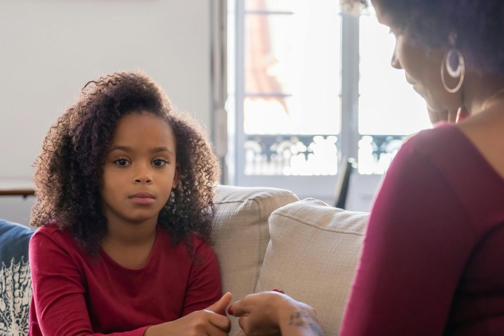 A mother and young daughter having a serious conversation on a couch at home
