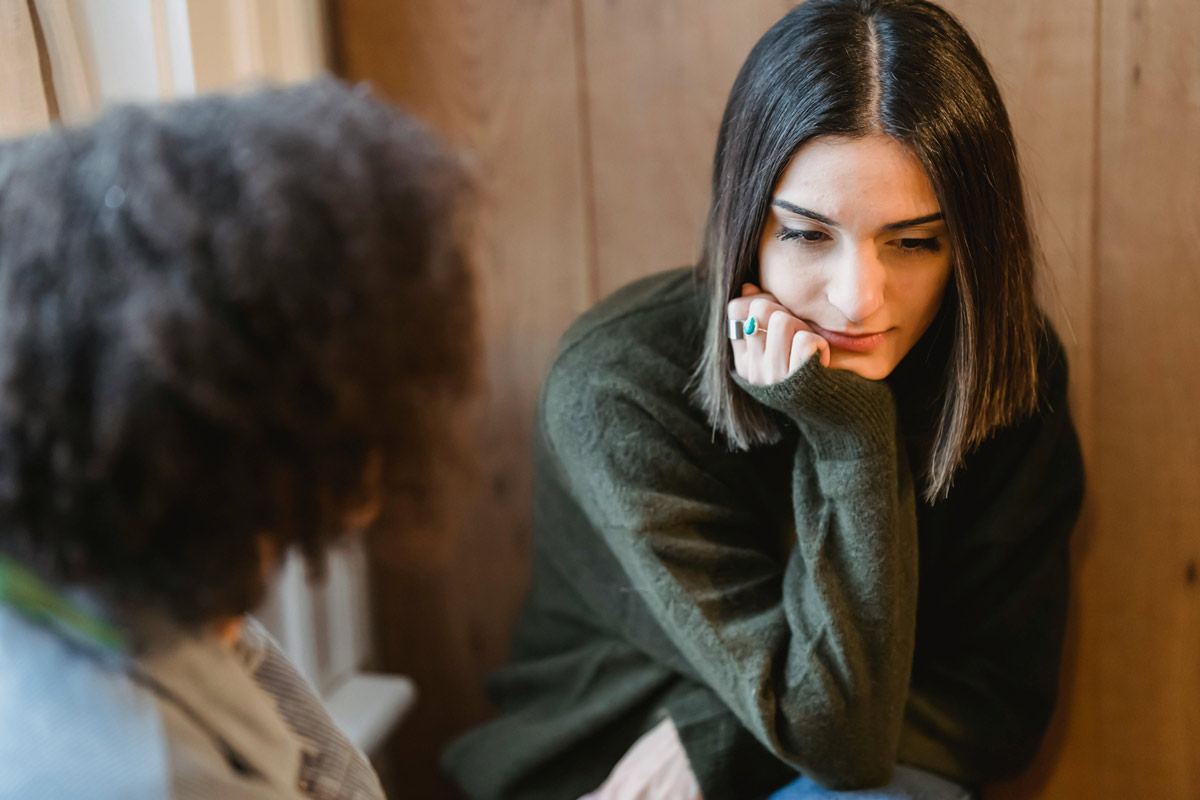 A woman listening with concern as someone shares a difficult experience, representing support for kratom dependence.