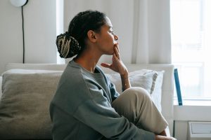 A woman sits quietly on a couch, hand to her chin, eyes closed, in a moment of reflection, conveying the weight of managing a mental health condition in recovery.