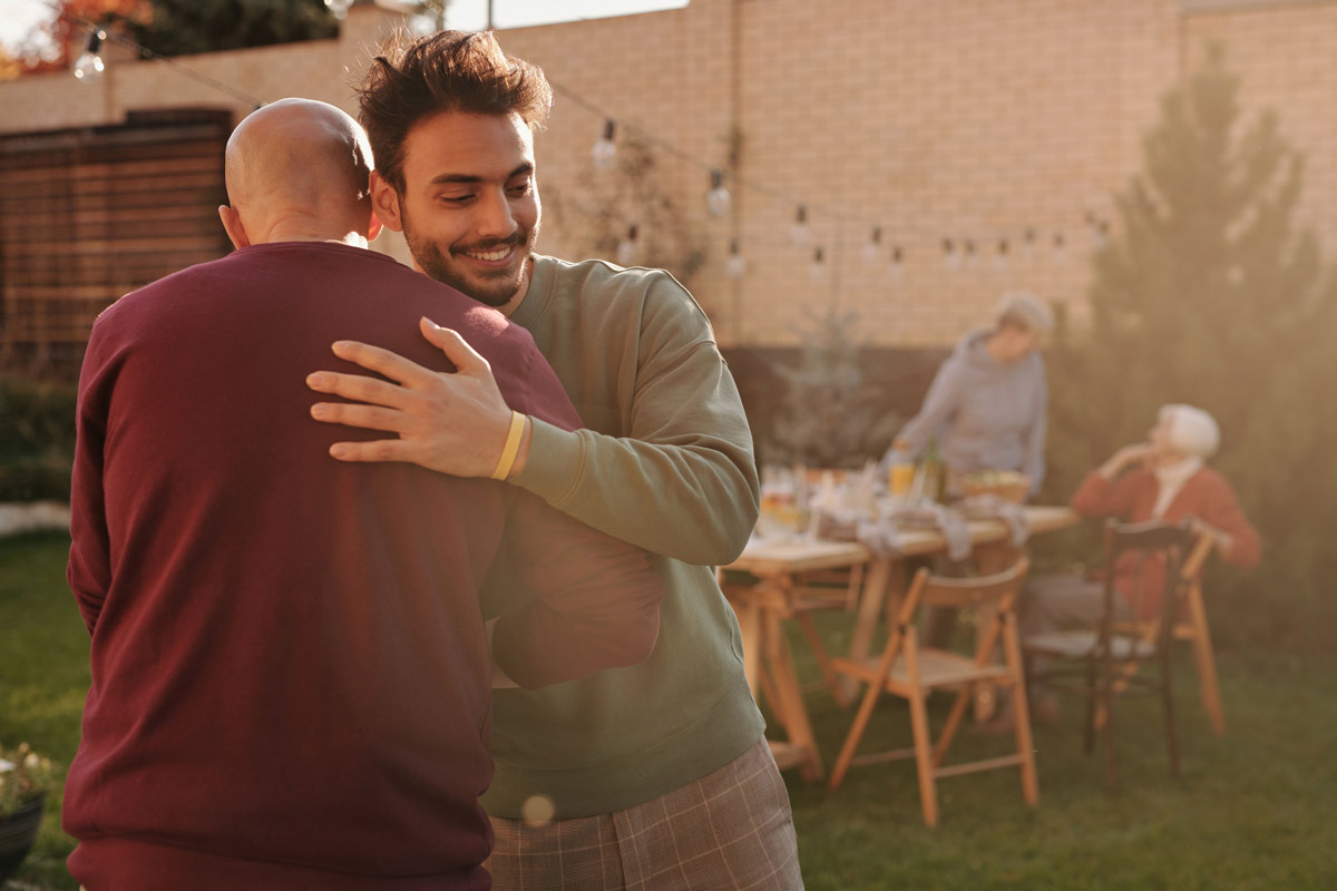 Two men embracing warmly at a family gathering outdoors.
