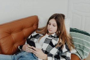 A teenage girl lying on a couch looking at her smartphone