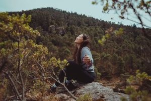 Woman sitting outdoors with eyes closed, face turned up, feeling free instead of shrinking herself.