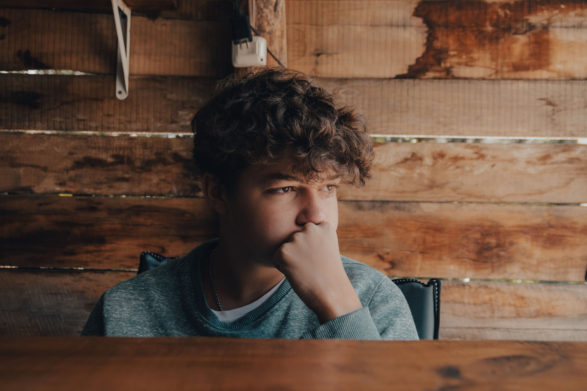 Teenage boy sitting at a table looking pensive and withdrawn.