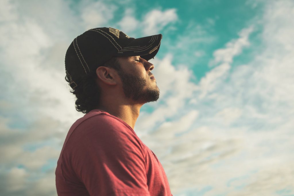 Man with eyes closed breathing calmly outdoors, practicing breathing exercises for anxiety.