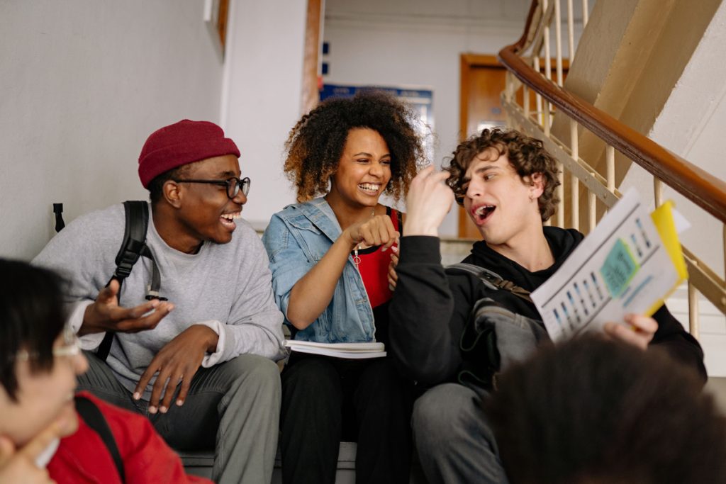 Group of college students sitting on stairs, laughing together while reviewing notes.