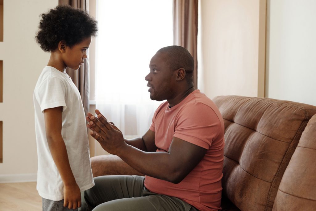Father crouching to talk calmly with his young son about OCD treatment.