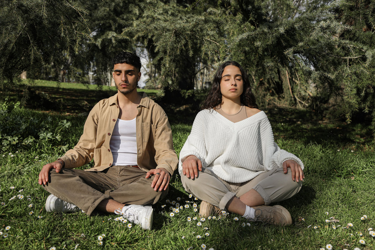 Man and woman practicing mindfulness meditation outside, sitting cross-legged with eyes closed.