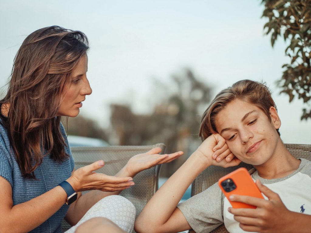 A mother tries to talk with her teen, who looks at a phone, showing the communication gap between parents and teens.